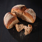 Aufgebrochenes Bauernbrot auf dunklem Tisch