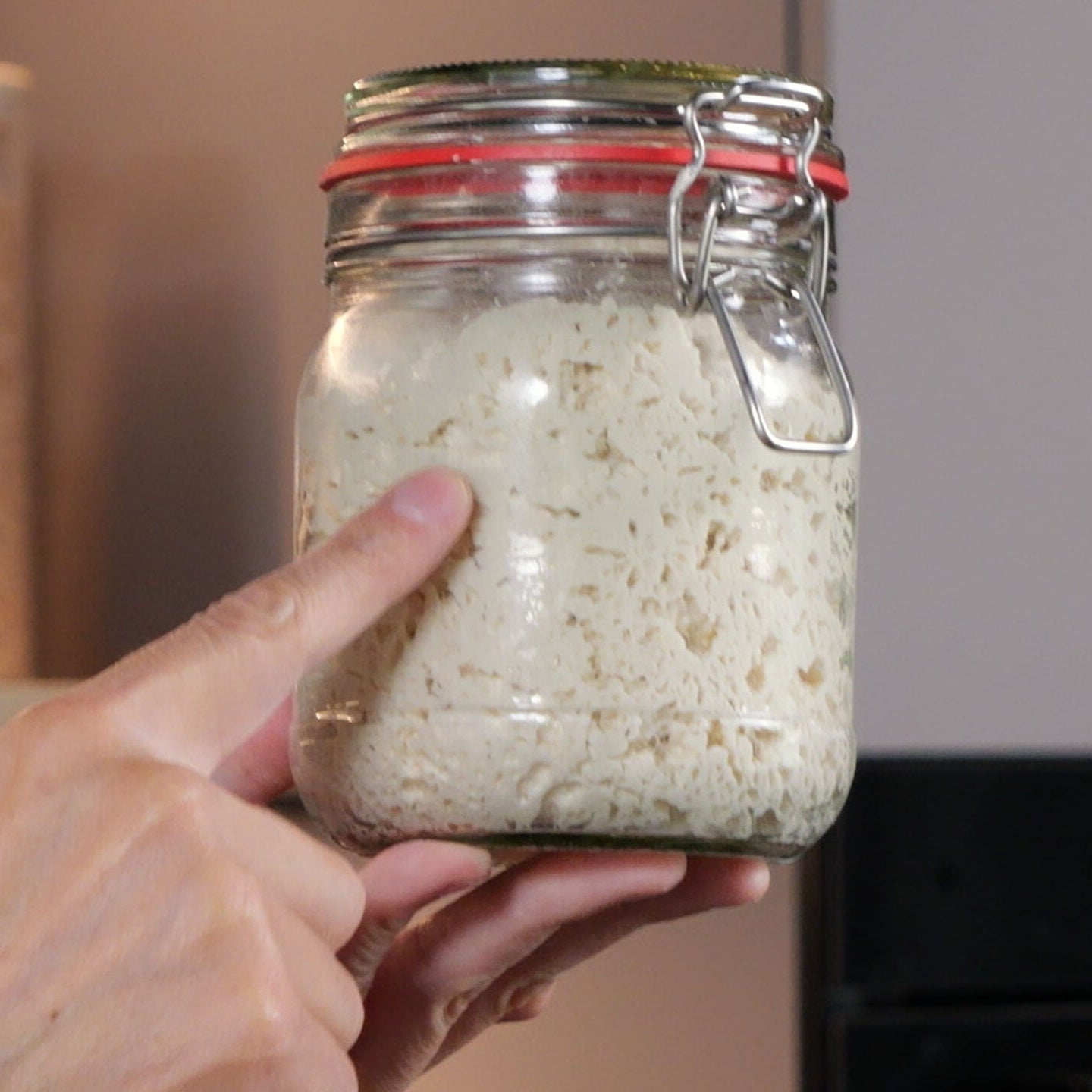 Hand hält Glas mit Sauerteig
