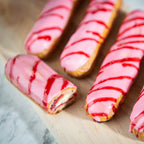 Vier pink glasierte Eclairs Holzbrett